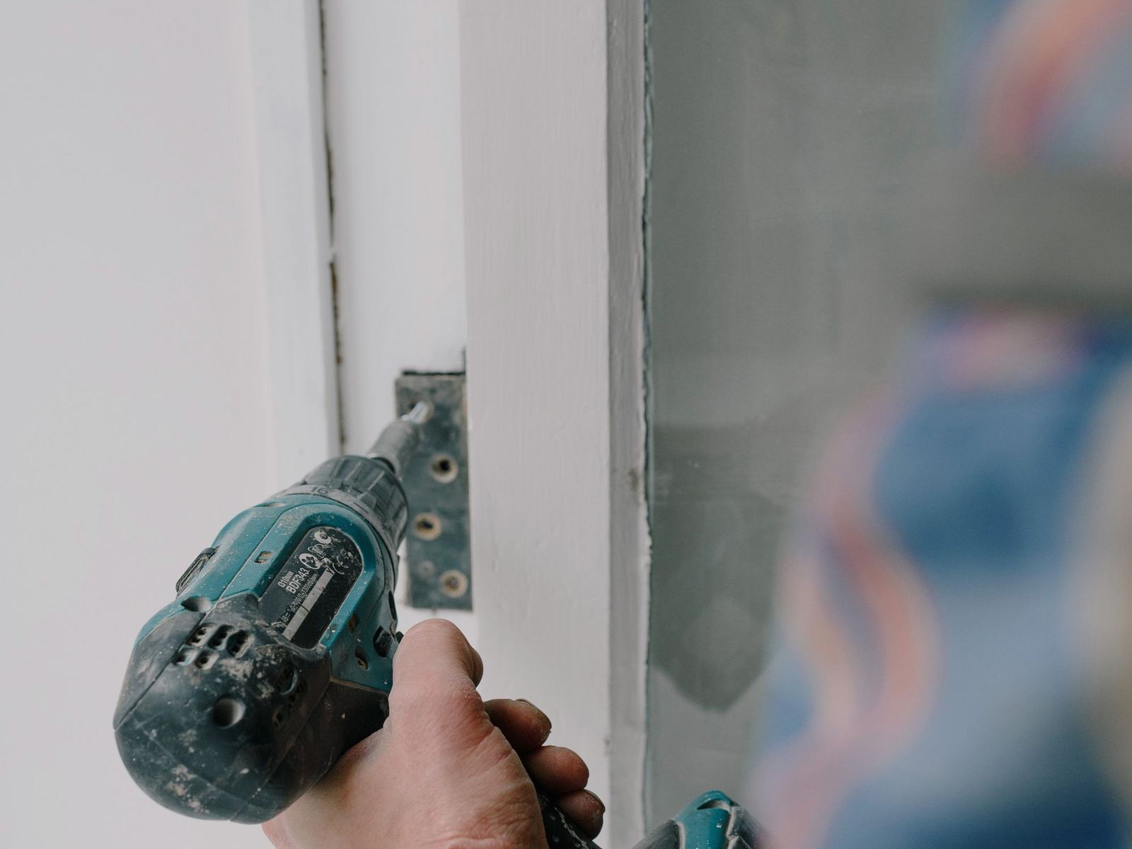Installateur vissant une charnière sur un cadre de fenêtre