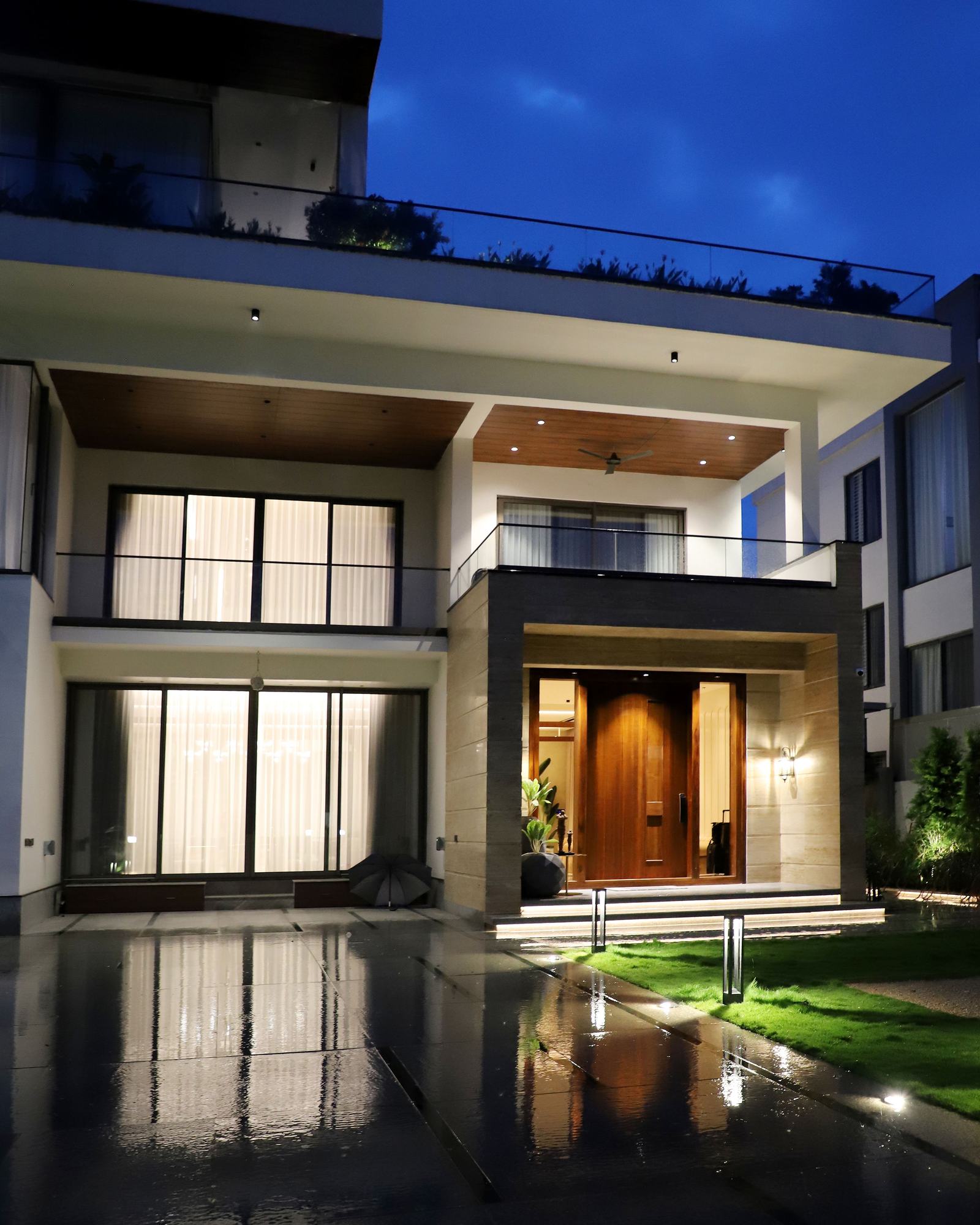 Villa contemporaine illuminée le soir, grandes baies vitrées et porte d'entrée en bois
